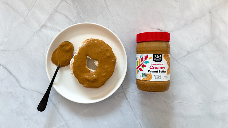 Peanut butter spread on a bagel next to a spoon and jar of 365 peanut butter
