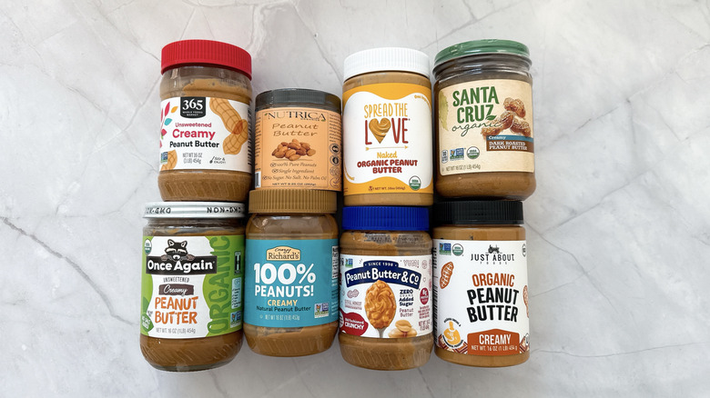 Eight jars of various peanut butter brands arranged on a marble counter
