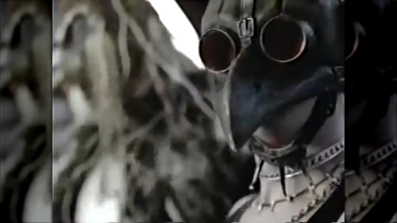 Still of person in creepy chicken-esque mask from Coq Rog commercial