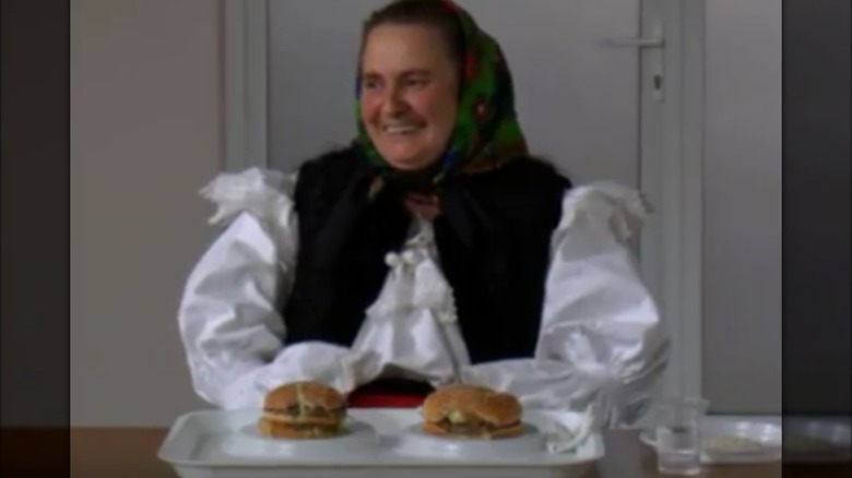 Woman in traditional Romanian dress sitting with two burgers