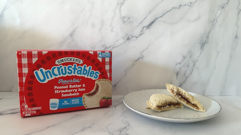 Uncrustables Strawberry box next to sandwich cut in half on white plate