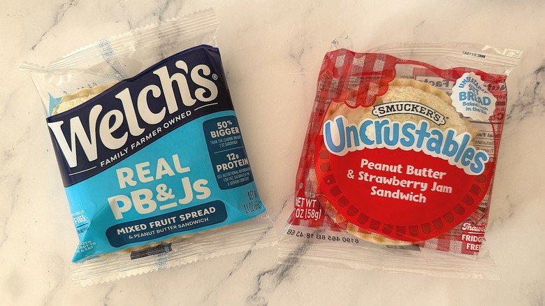 Packaged Welch's Real PB&J next to packaged Uncrustables PB&J on marble surface