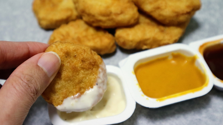 A person dipping chicken nuggets in various sauces