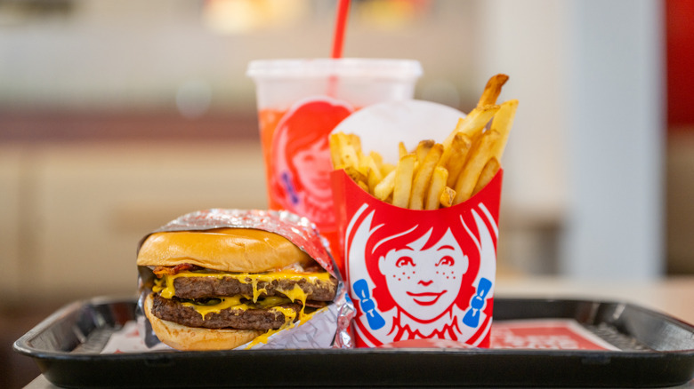 A Wendy's Double Cheeseburger extra some fries with a drink in the background on a tray