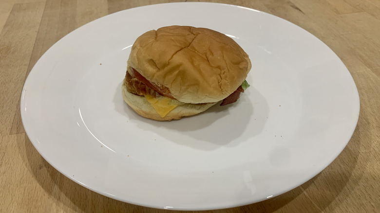 Chicken BLT sandwich on white plate on wood table