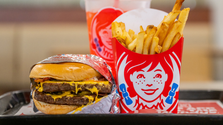 Wendy's meal on a plastic tray featuring French fries, a drink, and a double hamburger covered in cheese