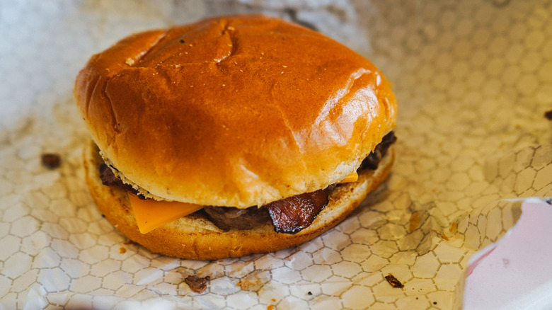 Small fast food cheeseburger with bacon sitting atop its wrapping