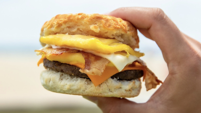 hand holding a biscuit sandwich with egg, bacon, cheese and sausage