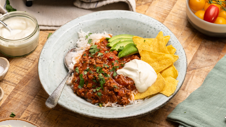 West Texas chili in a bowl topped with cream, avocado, and tortilla chips