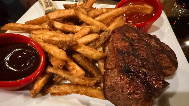 Steak with fries on plate with BBQ and ketchup
