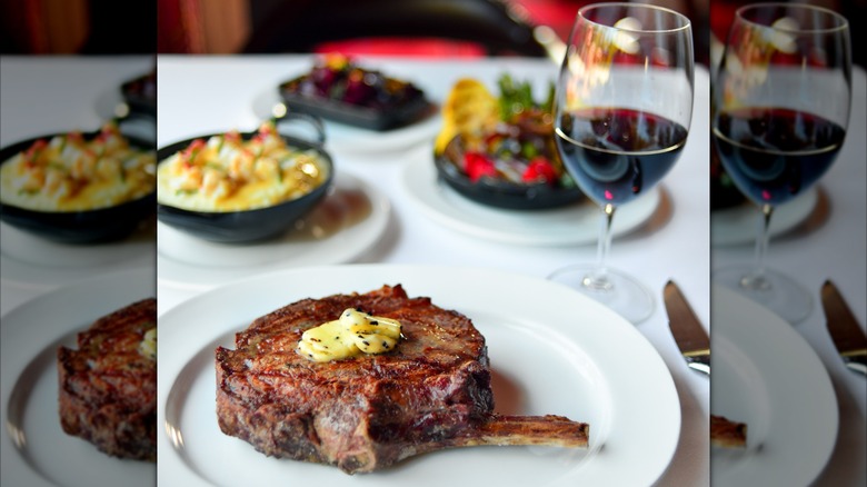 Steak on plate with glass of red wine and side dishes blurred in background