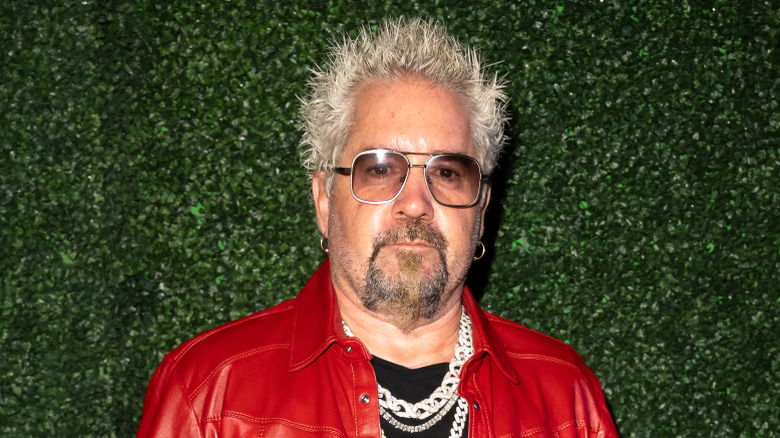 Guy Fieri standing in front of greenery backdrop