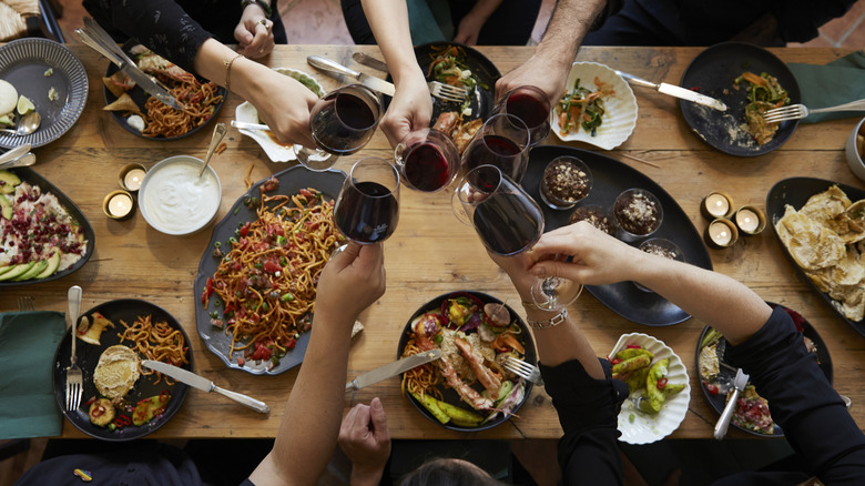 Diners clink glasses of red wine over plates of food