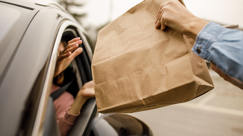 View of employee handing bag of groceries to customer through car window