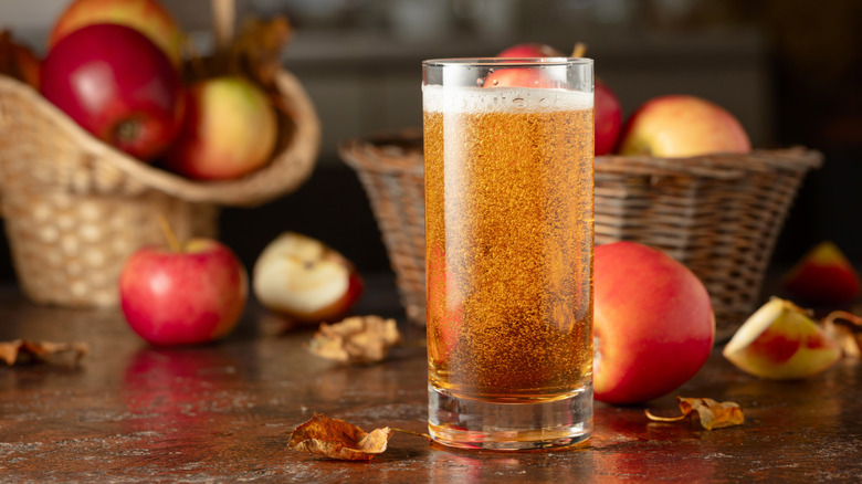 Glass of cider in front of apple baskets on wooden table