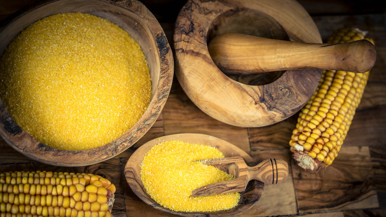 Bowls full of cornmeal alongside mortar and pestle and two corn cobs