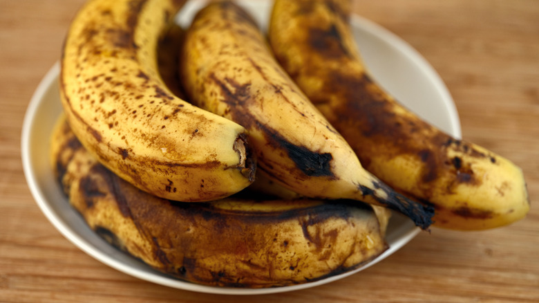A plate of over ripened bananas sitting on a wooden table