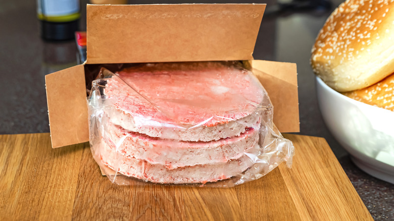 Frozen patties in a plastic covering coming out of a box.