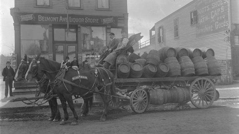A horse-drawn cart loaded up with beer barrels in front of a liquor store in the old west.