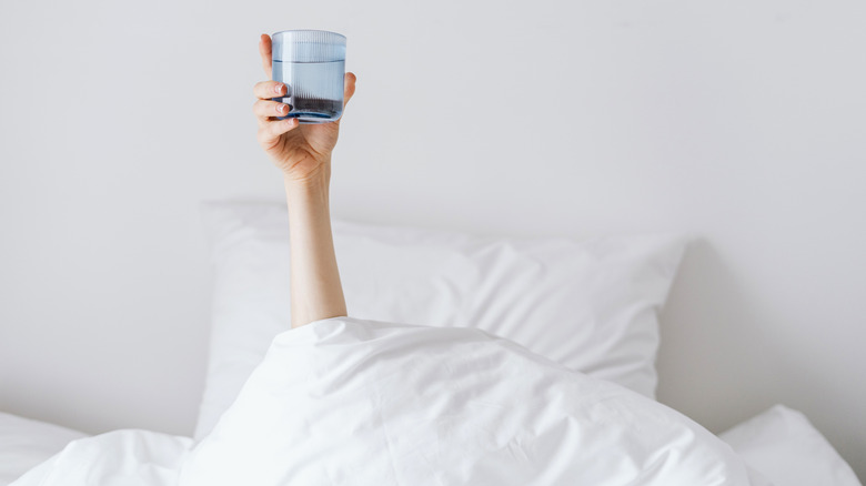 Person's hand holding a glass of water in bed