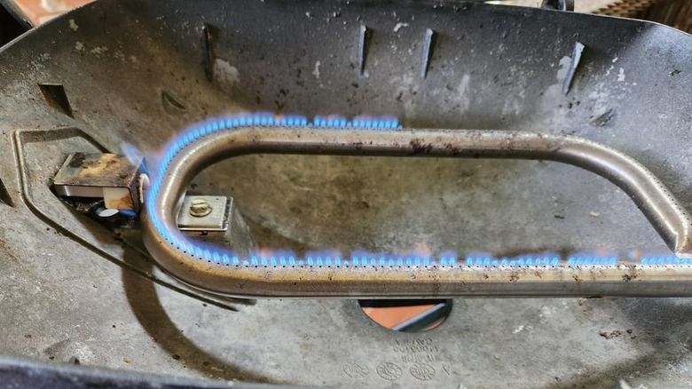 A close-up view of lit Weber grill burners with clogged ports that are only operating at half output