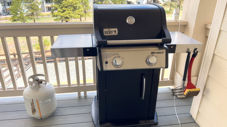 A Weber Spirit propane grill on a balcony next to a propane tank