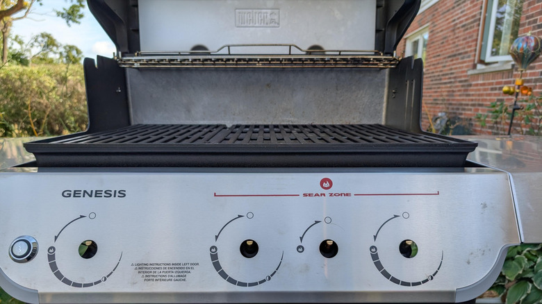 An open Weber Genesis grill with four burner control knobs