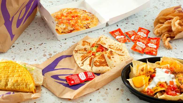 Various Taco Bell items on stone surface including Crunchwrap, Mexican Pizza, and nachos