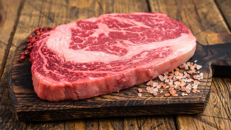 Fresh raw ribeye steak with rich marbling on a wooden cutting board and Himalayan rock salt