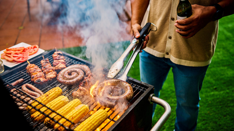 person cooking sausage corn and chicken on grill
