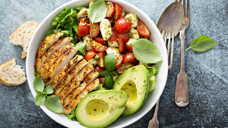 Overhead view of bowl of salad with chicken, avocado, and veggies