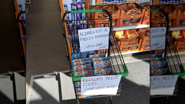 Shopping cart full of discounted food at a Dollar Tree store with handwritten signs in Spanish and English advertising they are reduced price