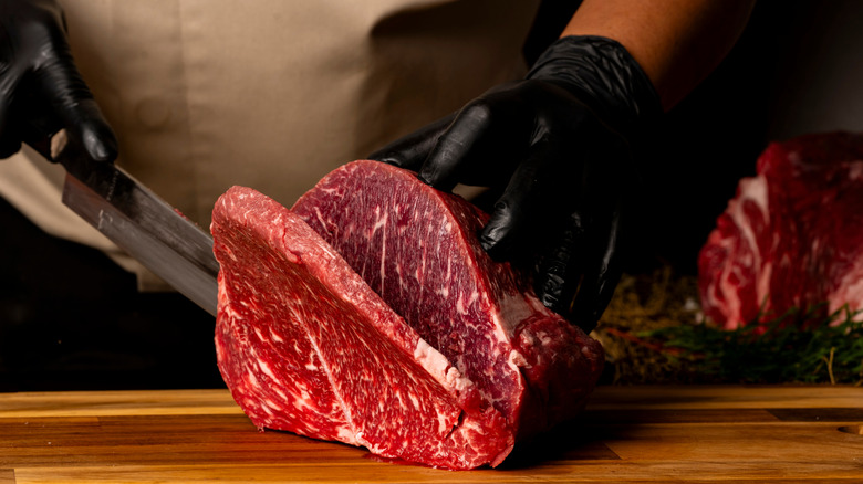 A person cuts a steak off of a large cut of meat