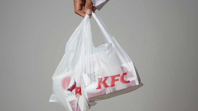 Hand holding a KFC branded plastic bag with KFC food and drink inside