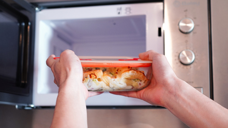 Person puts sealed container of leftovers in microwave.