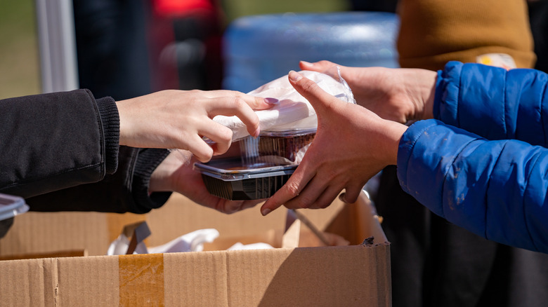 One person handing another a takeout container and plastic silverware
