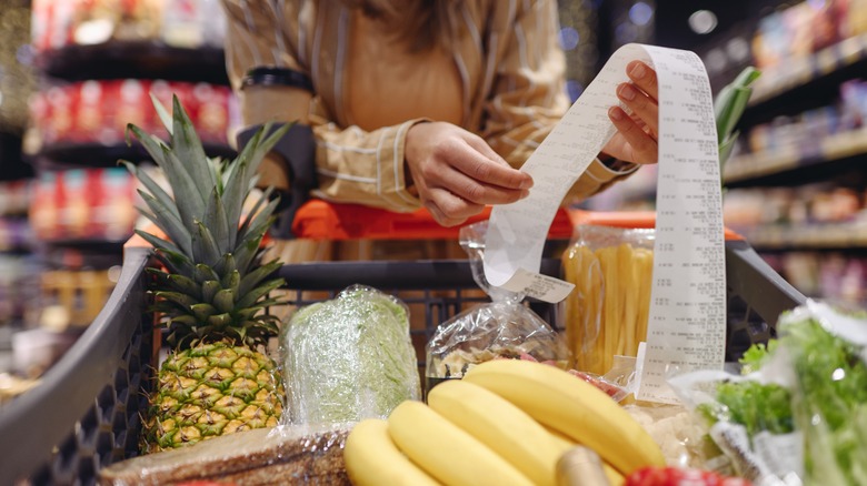 Woman looking at grocery bill with a cart full of food