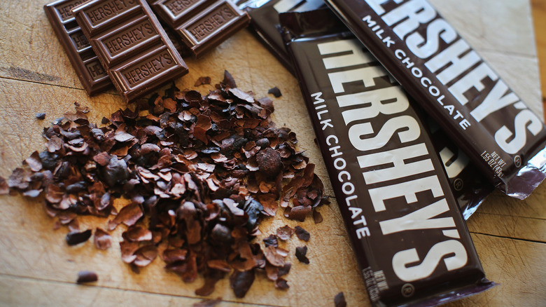 Wrapped Hershey's Chocolate Bars sit beside once that's been broken into pieces and one that's been grated on a wooden table