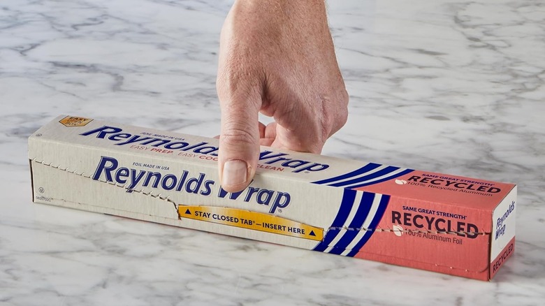 A hand holding box of Reynolds Wrap Recycled Foil on a marble counter