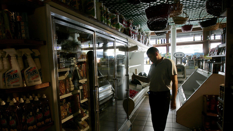 A grocery store employee stands in a darkened store looking at a cabinet of refrigerated food during a power outage
