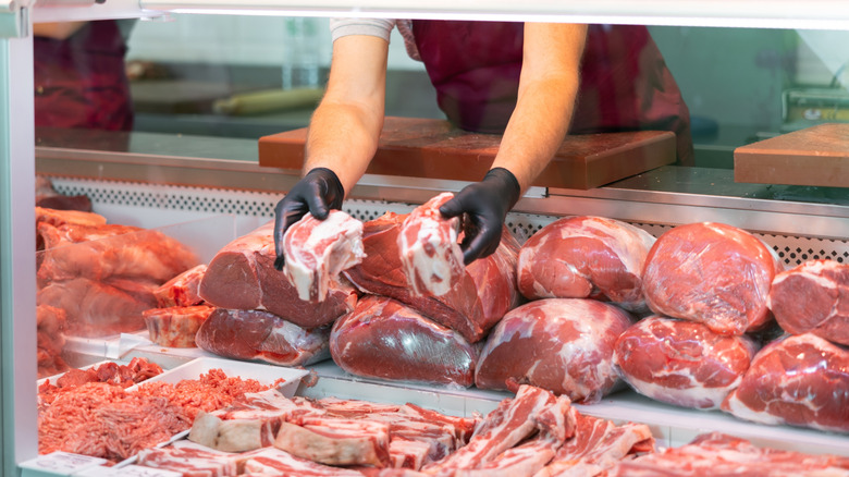 A butcher holds short ribs in a meat case