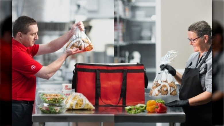 Chick-fil-A workers packaging leftover food in a kitchen and placing it in a red to-go bag.