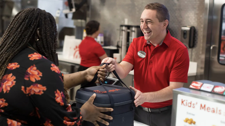 A Chick-fil-A worker in a red polo shirt donating leftover chicken to a person in a floral blouse.
