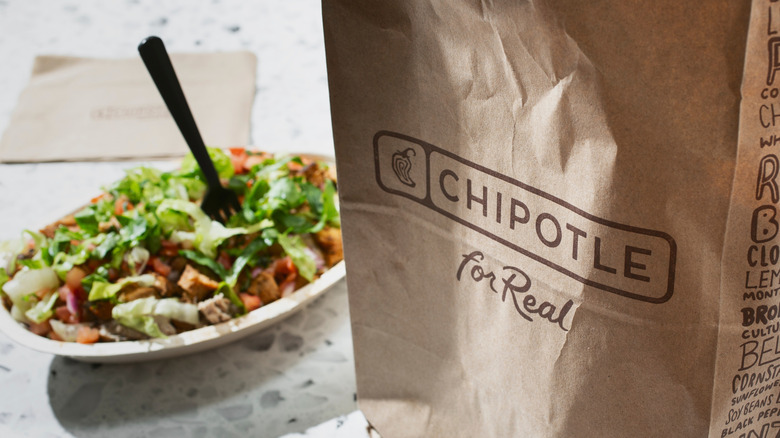 Chipotle burrito bowl with a fork sticking out, behind a paper Chipotle bag
