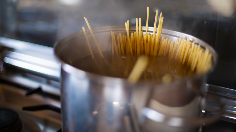 A boiling pot for pasta with what appear to be linguini noodles poking up out of the top of the water line in the pot