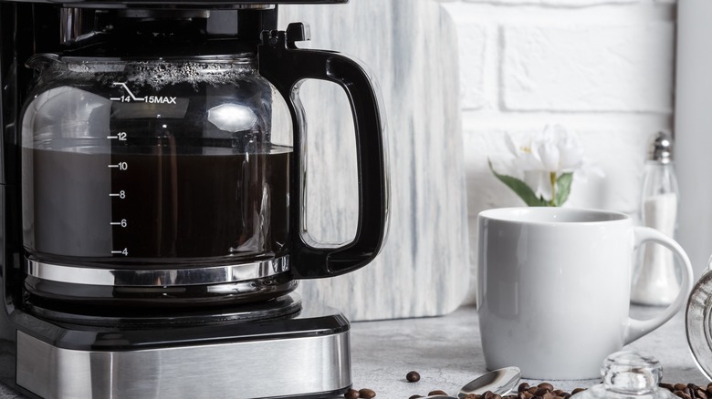 Drip coffee machine and white ceramic mug on counter