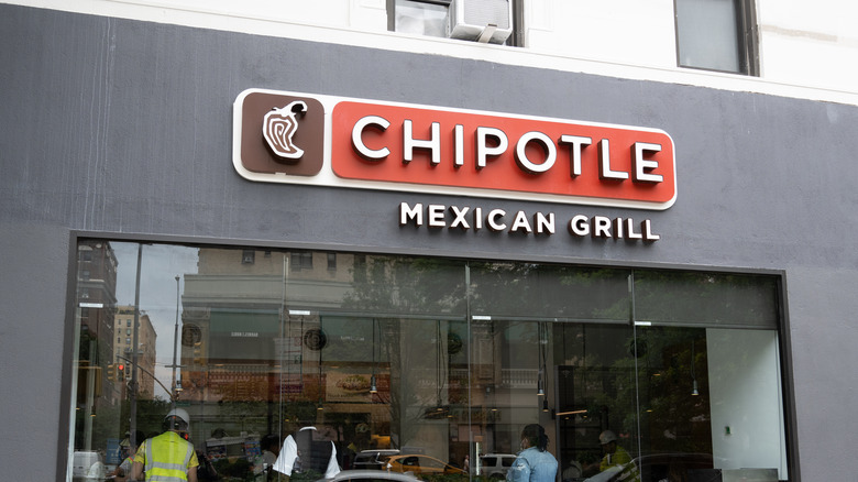 A grey Chipotle building with customers seen through a large window