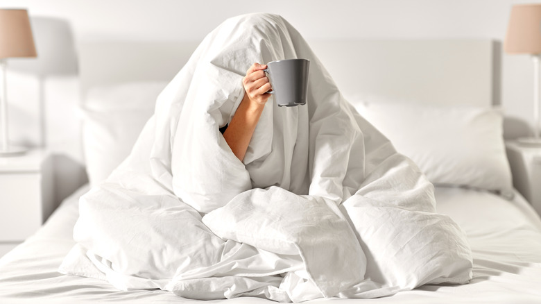 Person holding a mug of coffee in bed