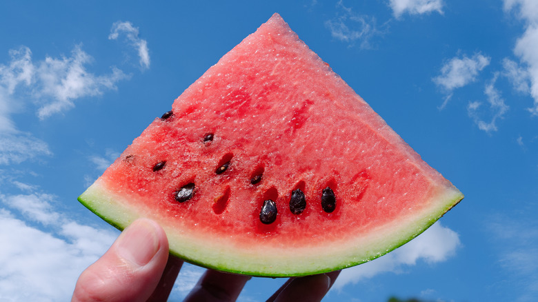 A piece of watermelon with black seeds held up to the sky