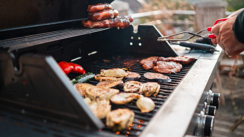 A person using tongs to flip food on a gas grill